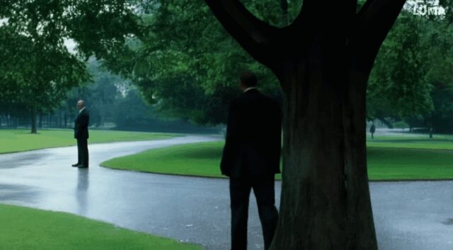 man with suit walks in the park on a rainy day, where he meets his twin brother. They shake hands.-156147