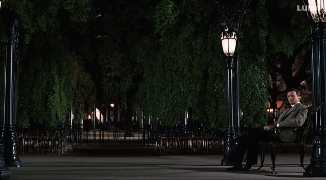 man with a suit walks in a park, he thh a suit sitting on a bench that looks exactly like him.