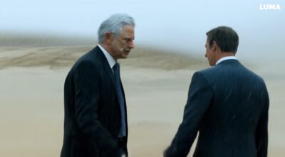 man with gray hair wearing a suit, walks in the dessert on a rainy day and meet his doppelgänger with grey hair and then they shake hands-fcd410