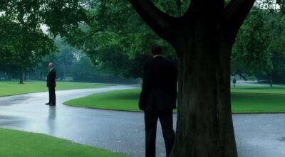 man with suit walks in the park on a rainy day, where he meets his twin brother. They shake hands.-156147