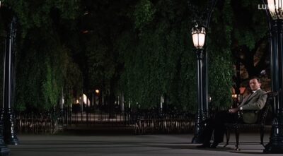 man with a suit walks in a park, he thh a suit sitting on a bench that looks exactly like him.