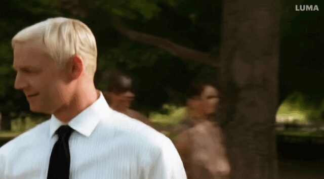man with a white shirt and black tie walks in the park were he meets another man with They then shake hands and walk away.-3913c6
